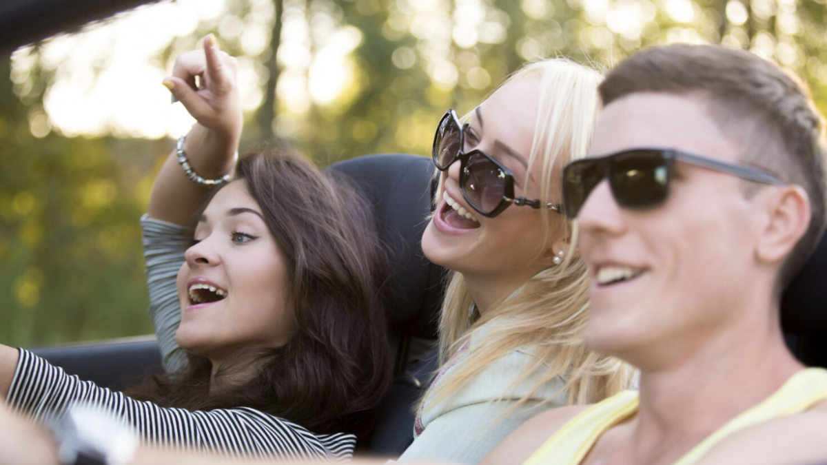 A group of teenagers laughing and enjoying themselves while driving in a car on a sunny day.