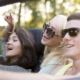 A group of teenagers laughing and enjoying themselves while driving in a car on a sunny day.