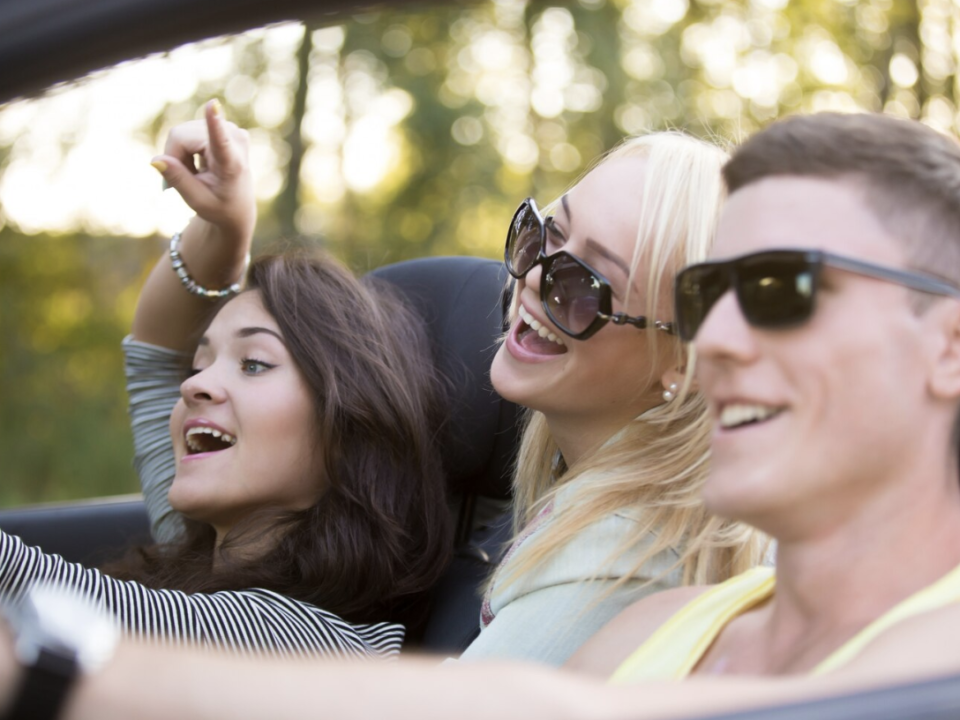 A group of teenagers laughing and enjoying themselves while driving in a car on a sunny day.
