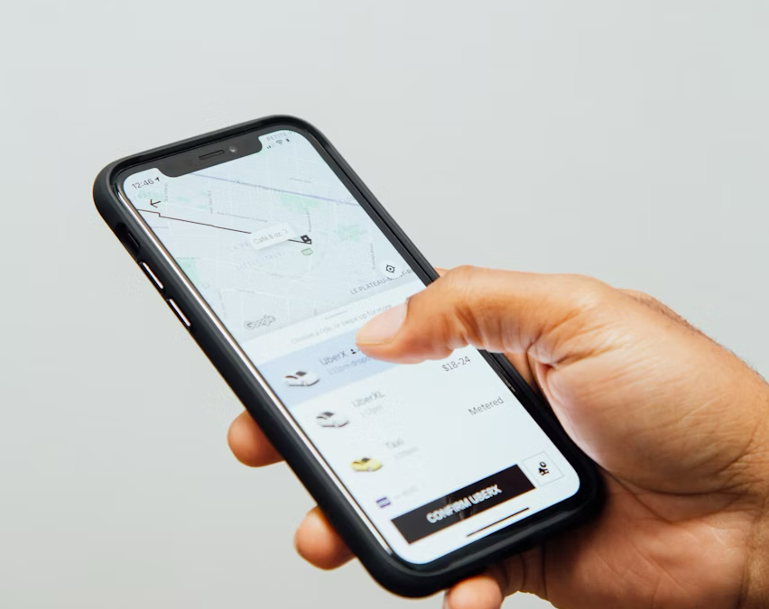A person's hand holding a smartphone, using a ride-sharing application like Uber to book a ride.