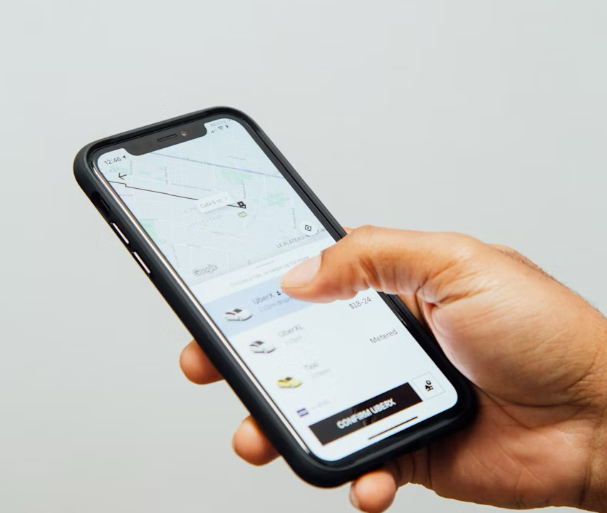 A person's hand holding a smartphone, using a ride-sharing application like Uber to book a ride.