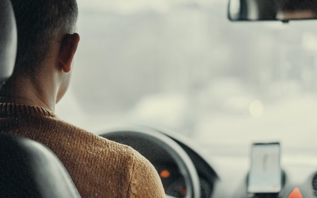 An Uber driver sitting in their vehicle, looking at their phone, likely waiting for or navigating to a passenger.