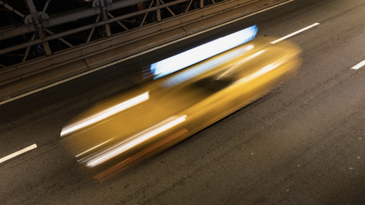 A blurred image of a car speeding across a bridge at night.