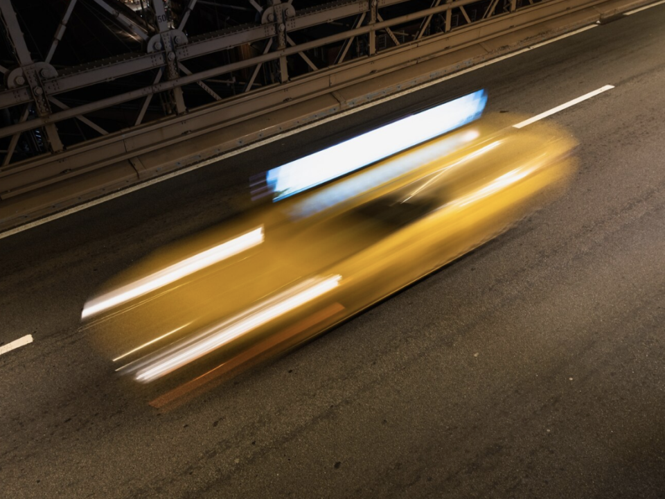 A blurred image of a car speeding across a bridge at night.
