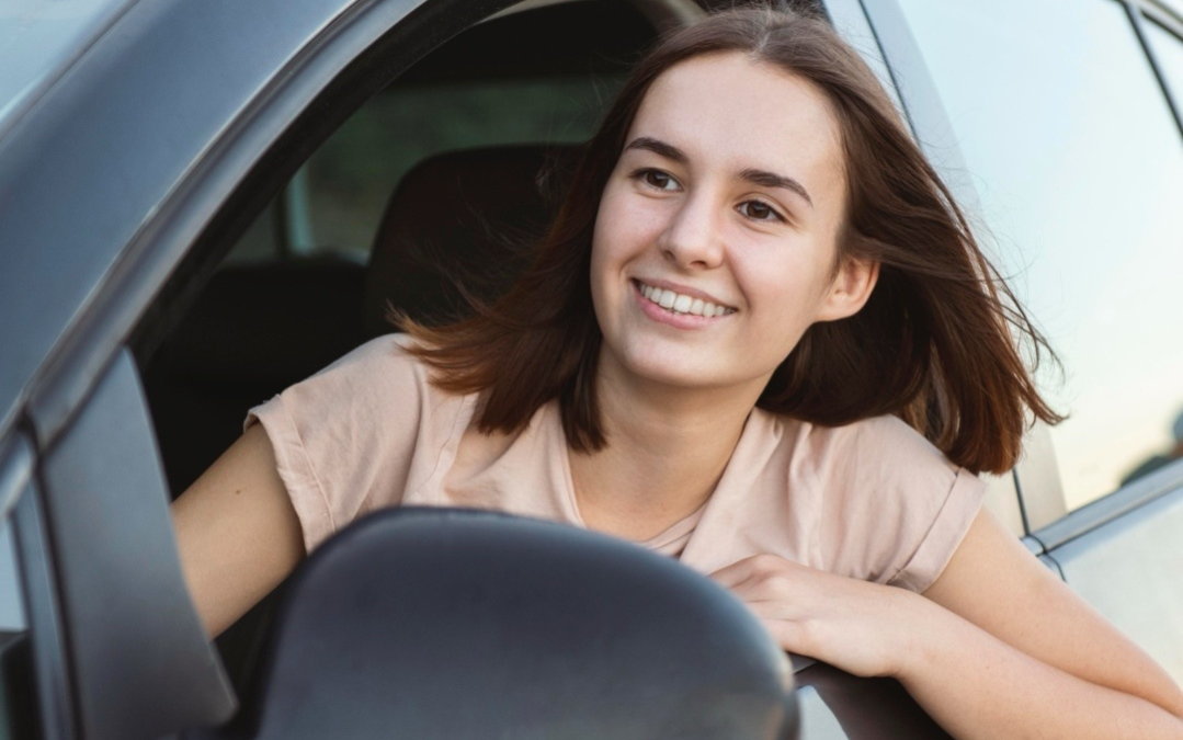 A smiling teenager driving a car.