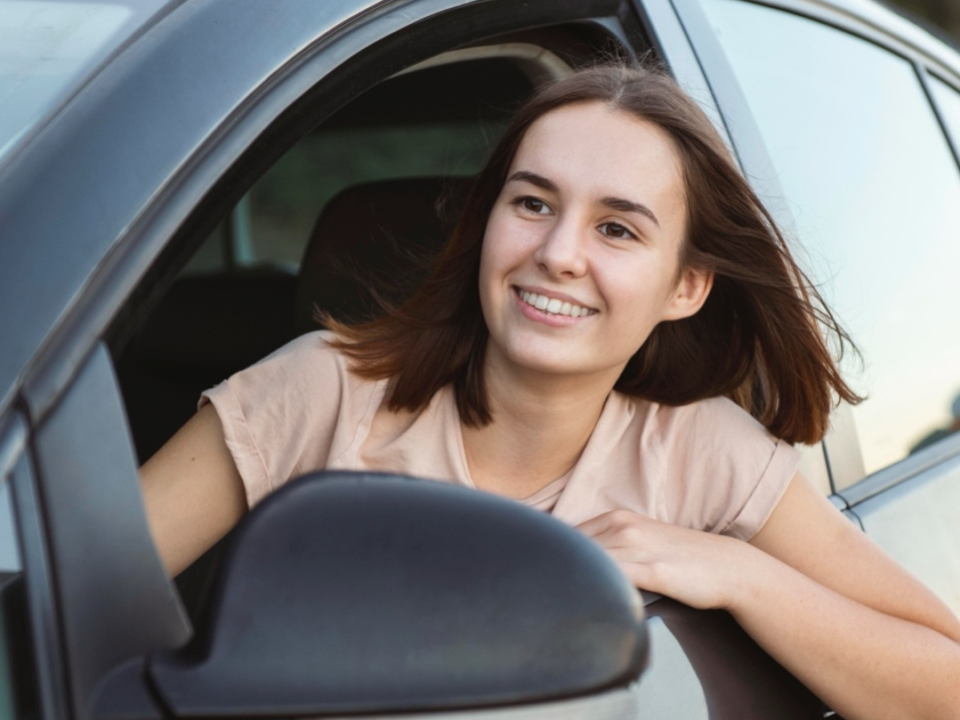 A smiling teenager driving a car.