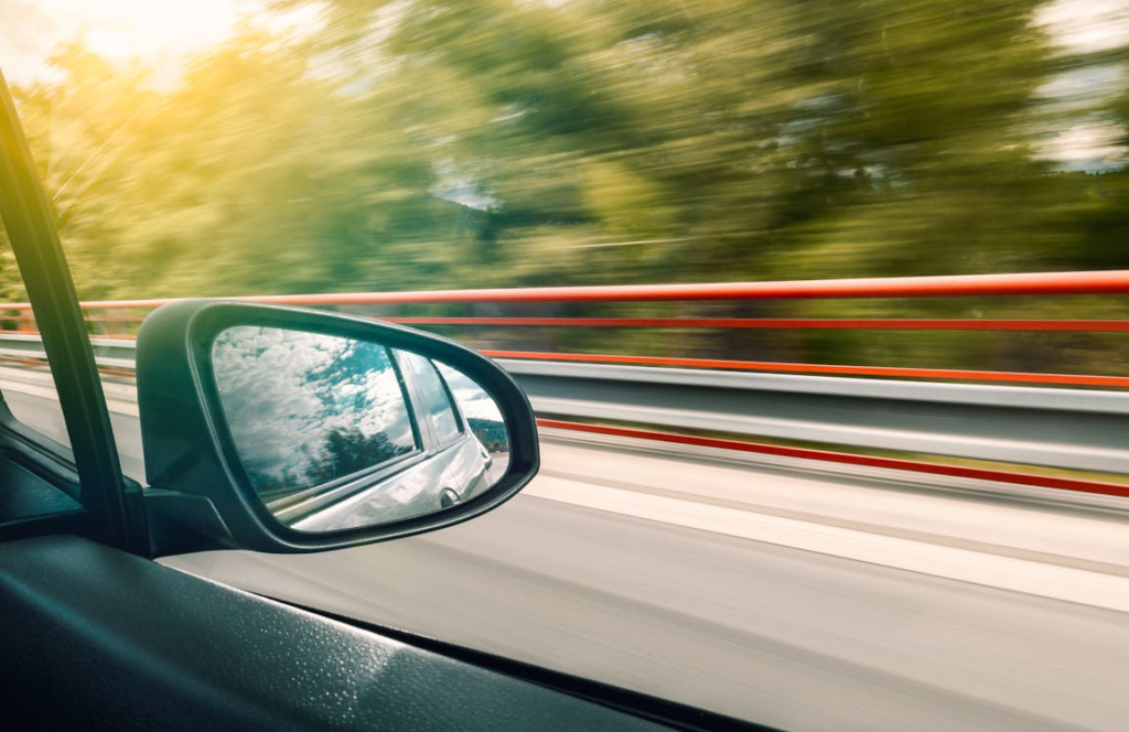 Black car side mirror reflecting a road and surrounding environment